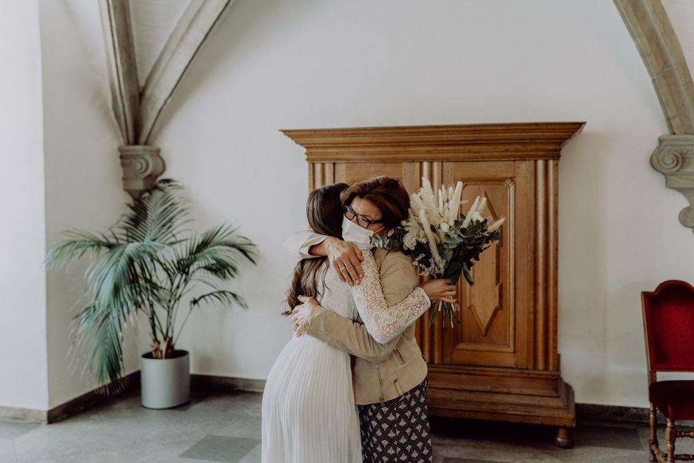 Intimate moment shared between two people in formal attire next to a wooden armoire and potted plants.