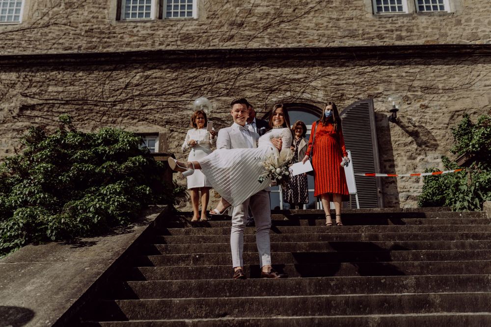 Wedding party poses on grand stone staircase outside historic building.