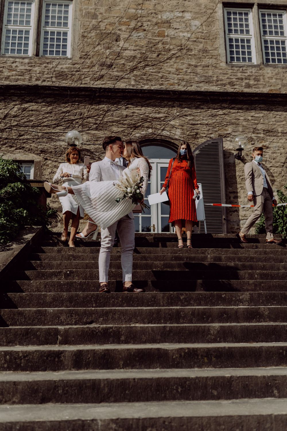 Celebratory scene on stone steps with wedding party in formal attire outside historic building.