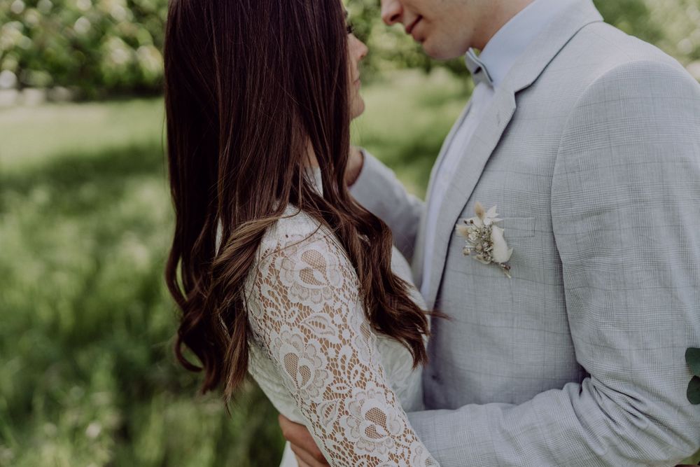 Close-up detail of lace wedding dress and light grey suit during an outdoor photoshoot.
