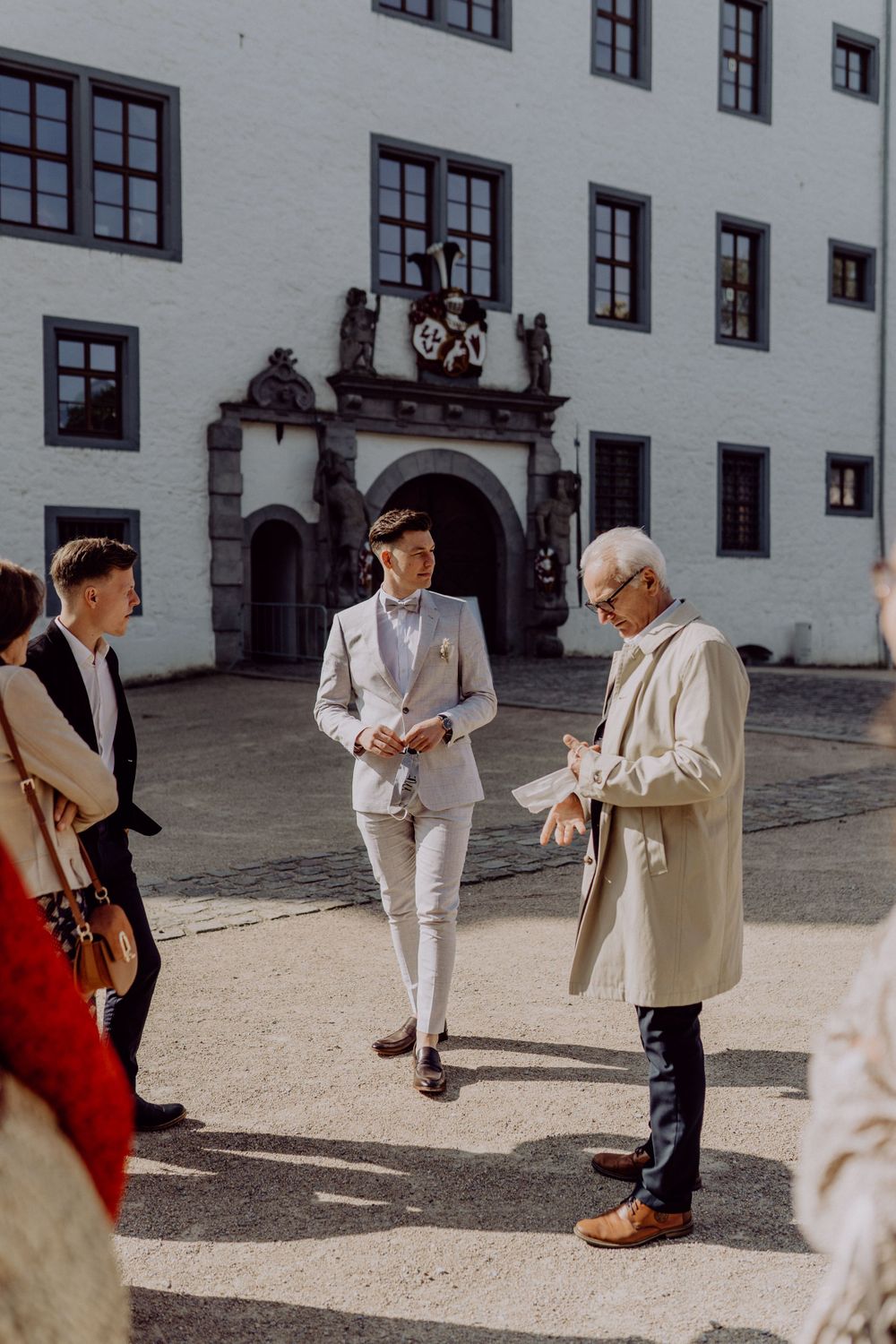 People gathered in a courtyard of a historic white building with ornate archway entrance.