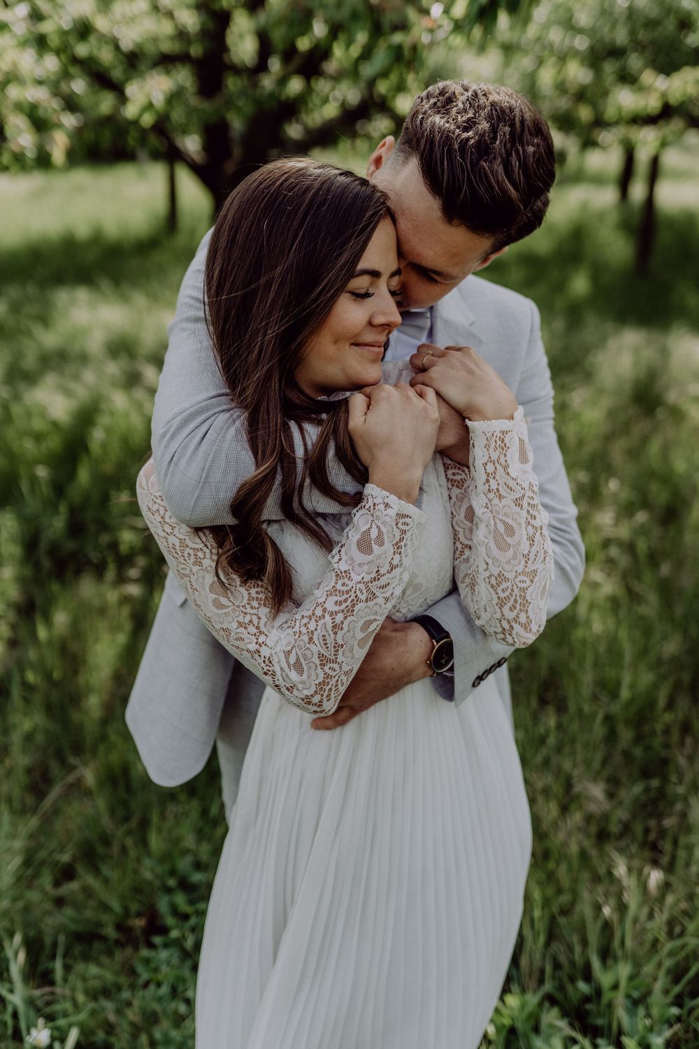 Intimate embrace between couple in wedding attire surrounded by spring greenery.