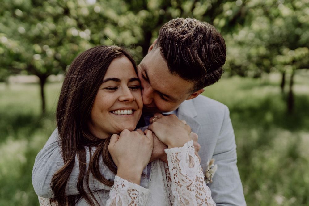 Intimate outdoor portrait of a couple sharing a joyful moment in white attire against a lush green backdrop.