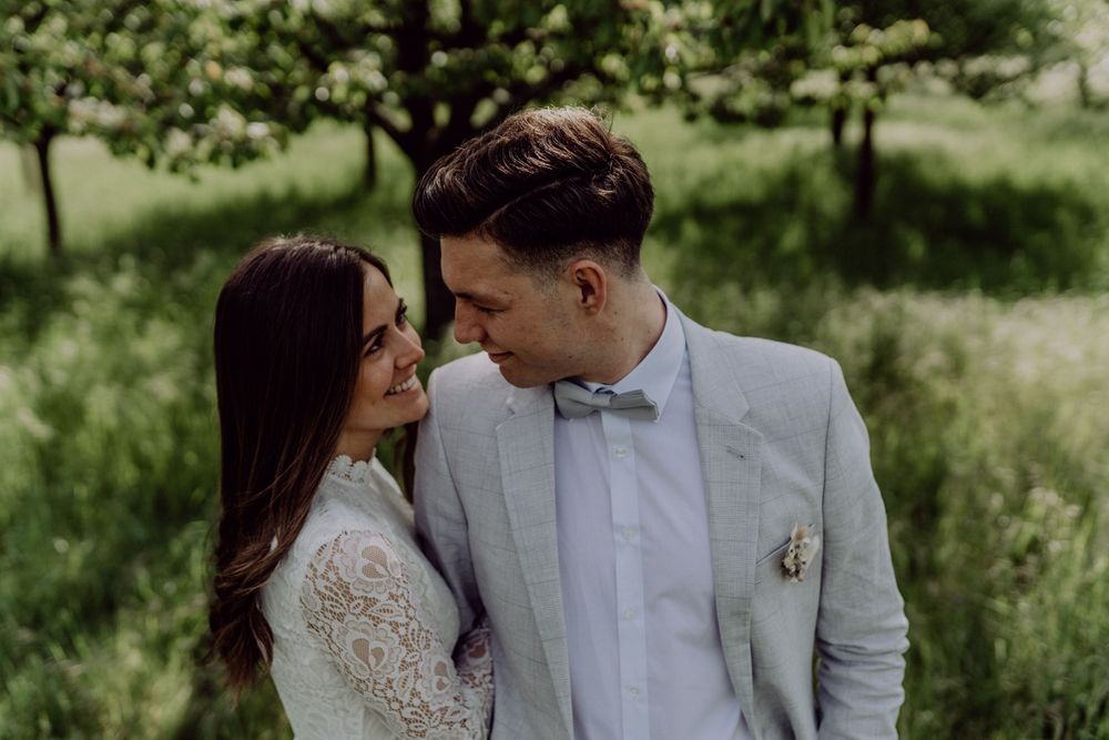 Romantic outdoor wedding portrait with couple in white lace dress and light grey suit with bowtie.