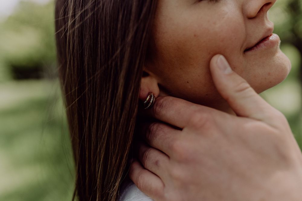Intimate close-up of gentle hand caressing face against natural green background.