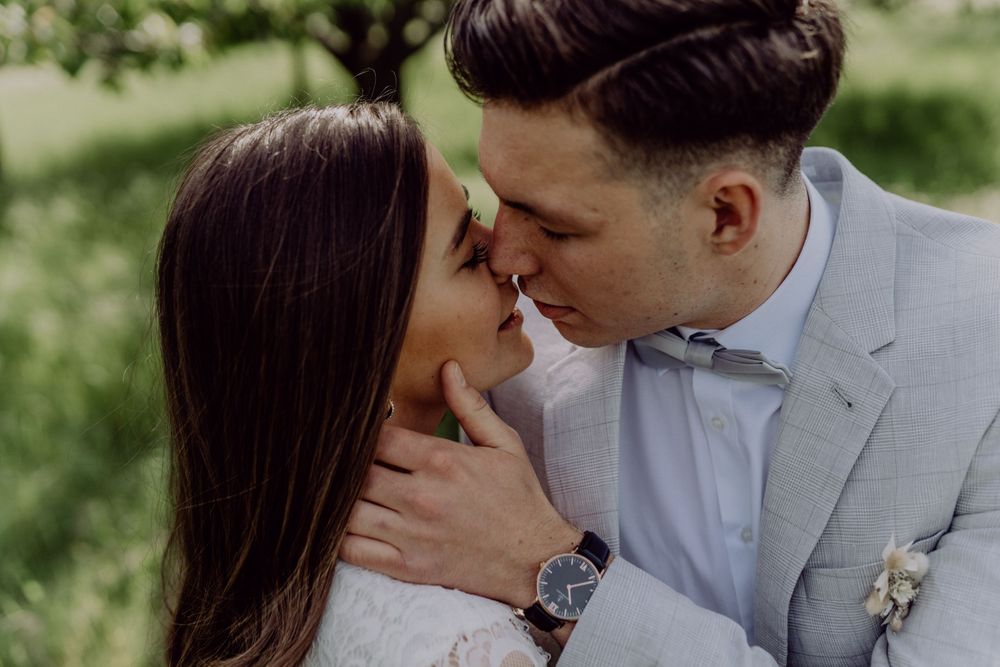 Romantic wedding portrait with couple sharing tender moment in light grey suit and white lace dress.