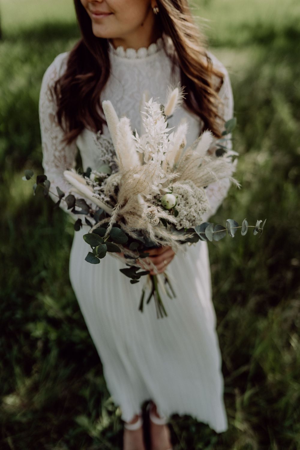 Close-up view of a delicate dried flower bouquet with pampas grass held against a white lace dress.