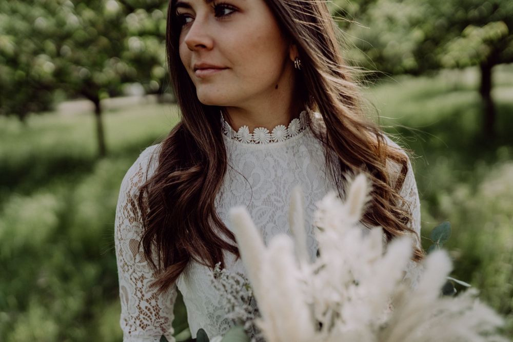 Side profile portrait showing lace high-neck detail of a white dress with pampas grass bouquet.