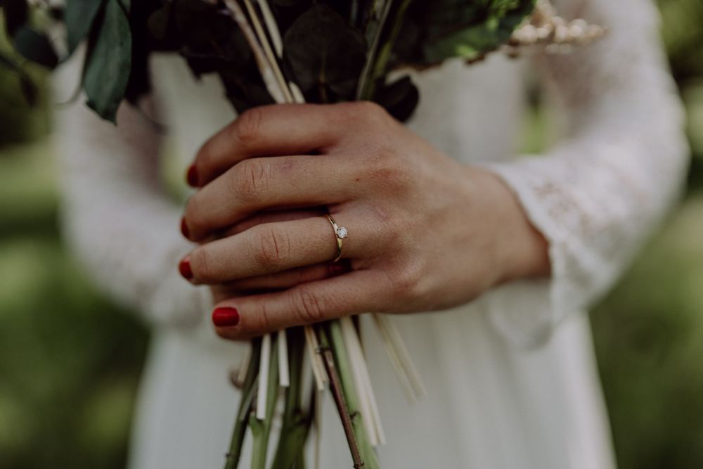 Close-up of hands holding a wedding bouquet with an engagement ring visible.