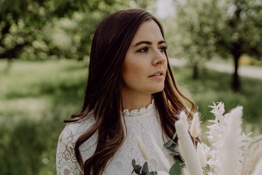 Elegant bridal portrait in a natural garden setting with dried floral bouquet.