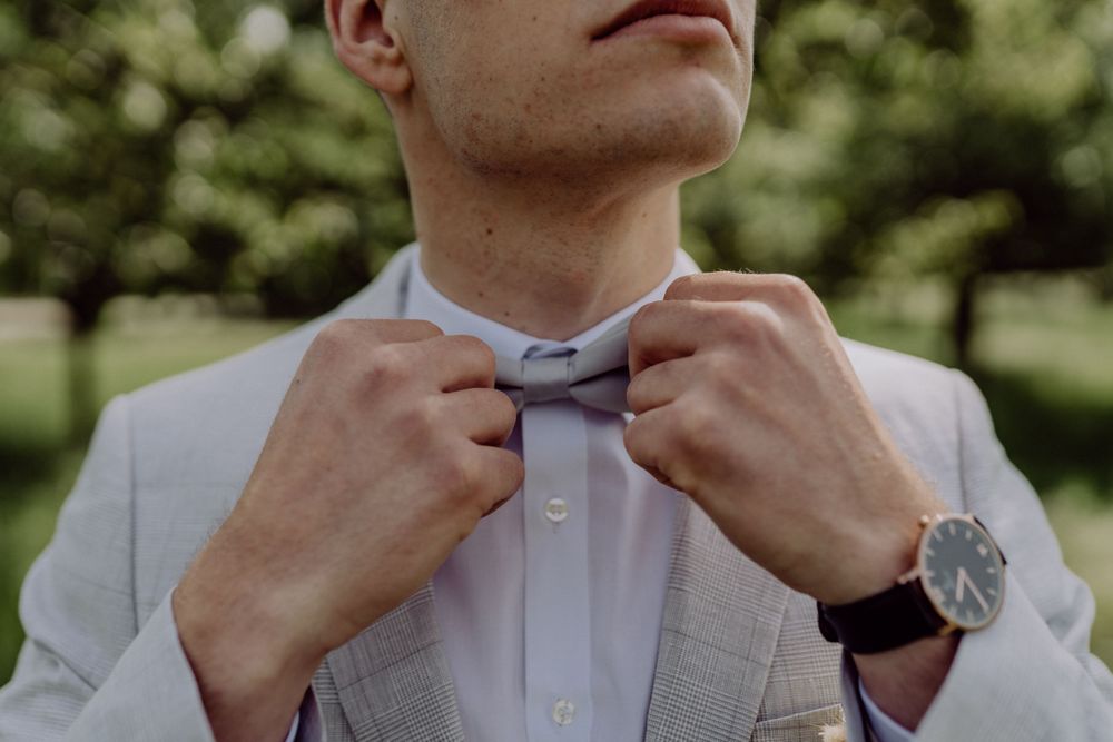 Close-up of hands adjusting a light gray bowtie with a watch visible.