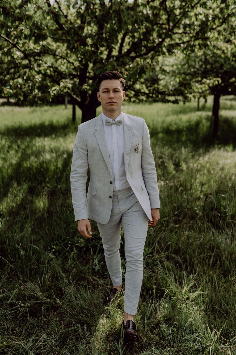 Full-length view of a light gray suit with bow tie in an outdoor garden setting.