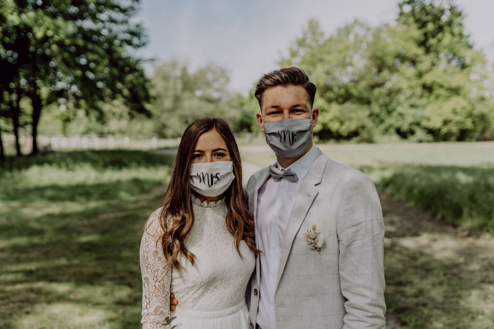 Couple in wedding attire wearing protective face masks in a garden setting.
