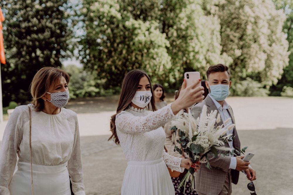 Wedding guests in face masks taking photos outdoors with smartphones.
