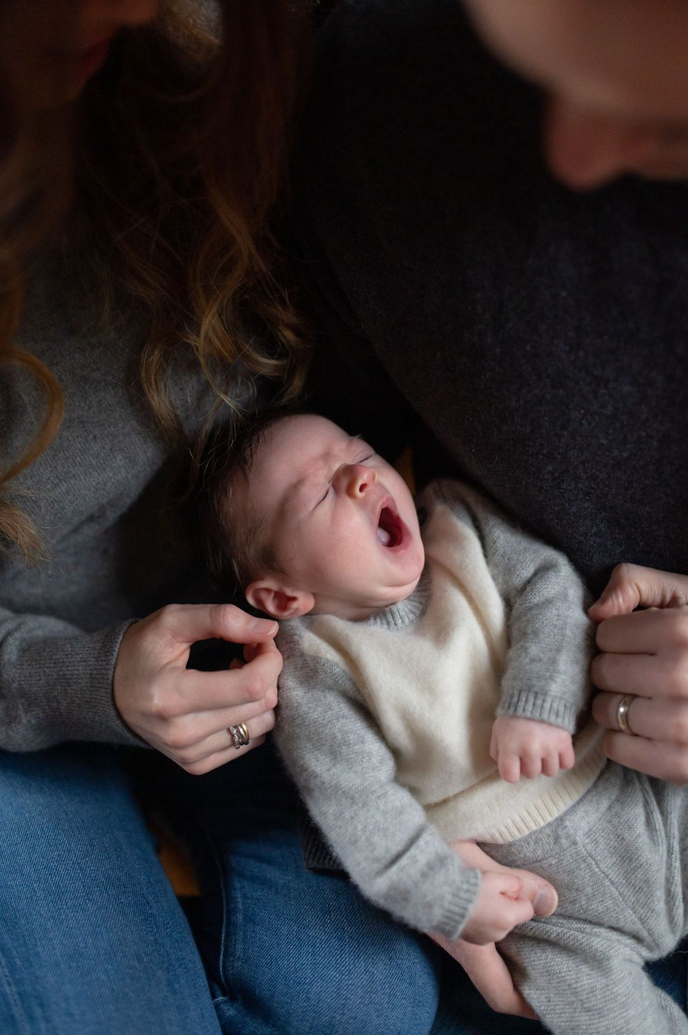 Baby yawning while being held in grey sweater on parent's lap.