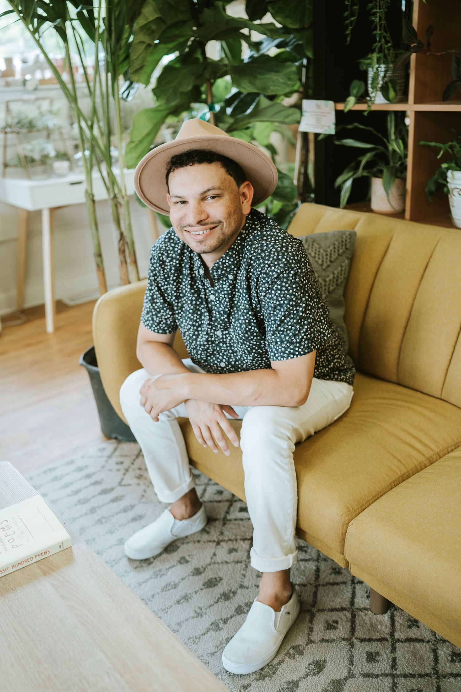Person in patterned shirt and hat relaxes on yellow couch in modern tropical-themed room.