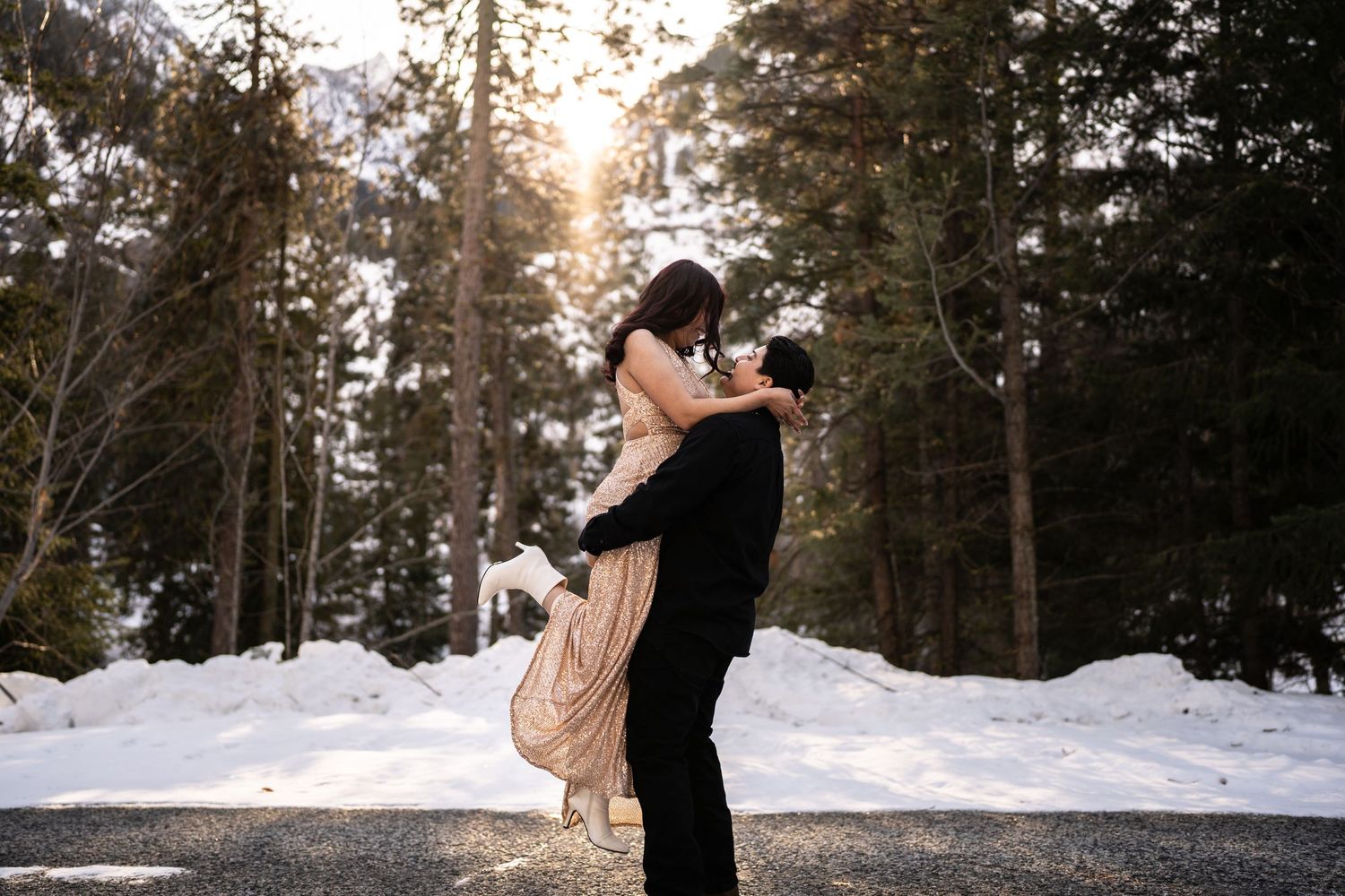 A romantic lift pose between a couple on a snowy forest road at sunset.