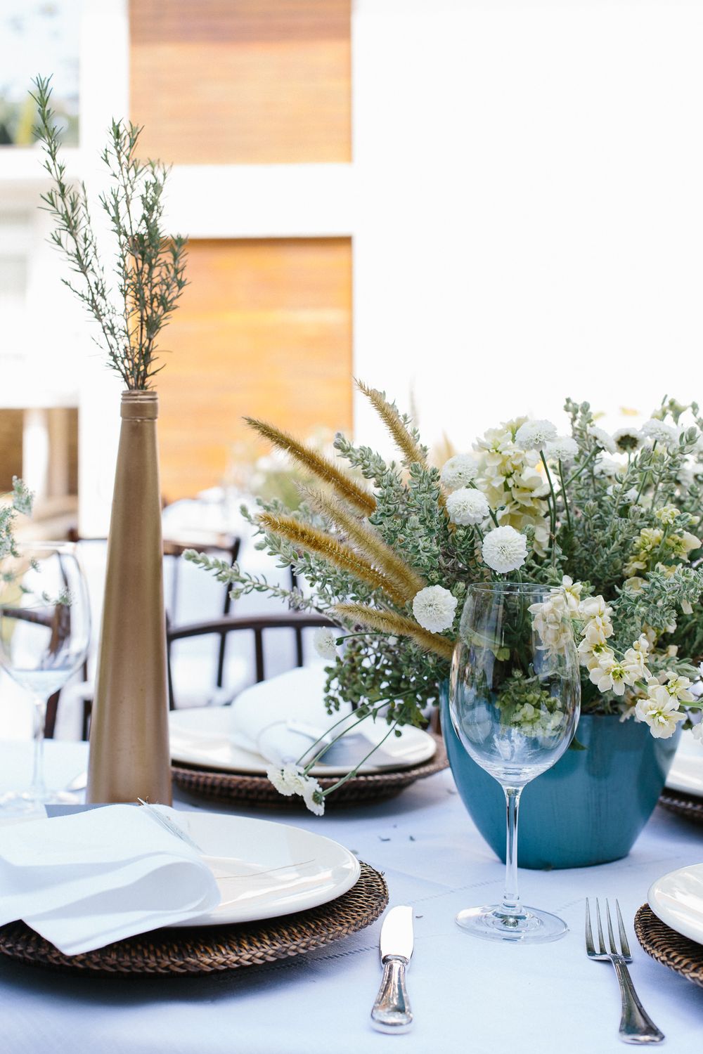 Elegant table setting with white flowers and greenery in blue vase.