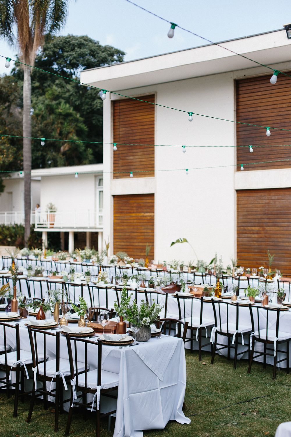 Modern wedding venue with long tables set up outdoors against white and wood facade.