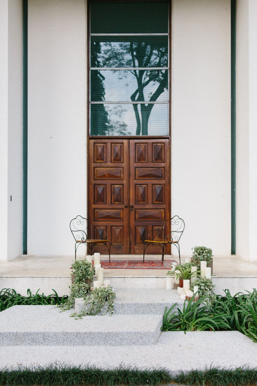 Elegant wooden door entrance with vintage metal chairs and white candles creating a welcoming ambiance.
