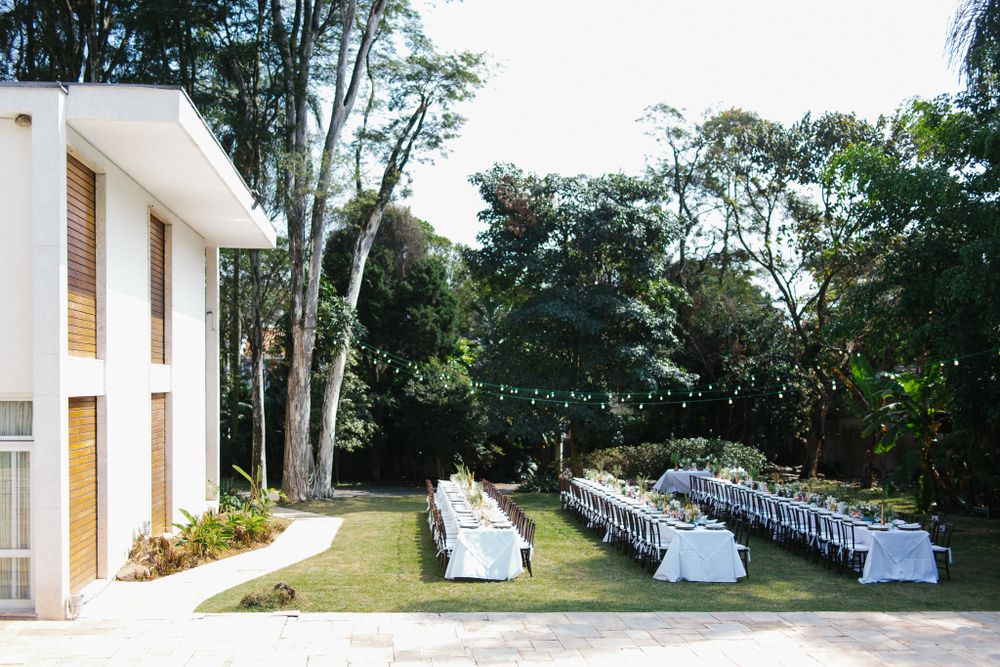 Outdoor wedding ceremony and reception setup with white chairs arranged on a lawn beside a modern building.