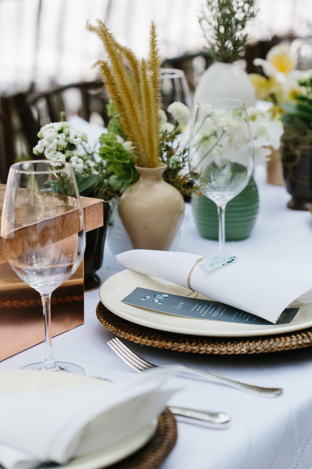 Detailed wedding place setting with woven charger, menu card, and mixed floral centerpieces.