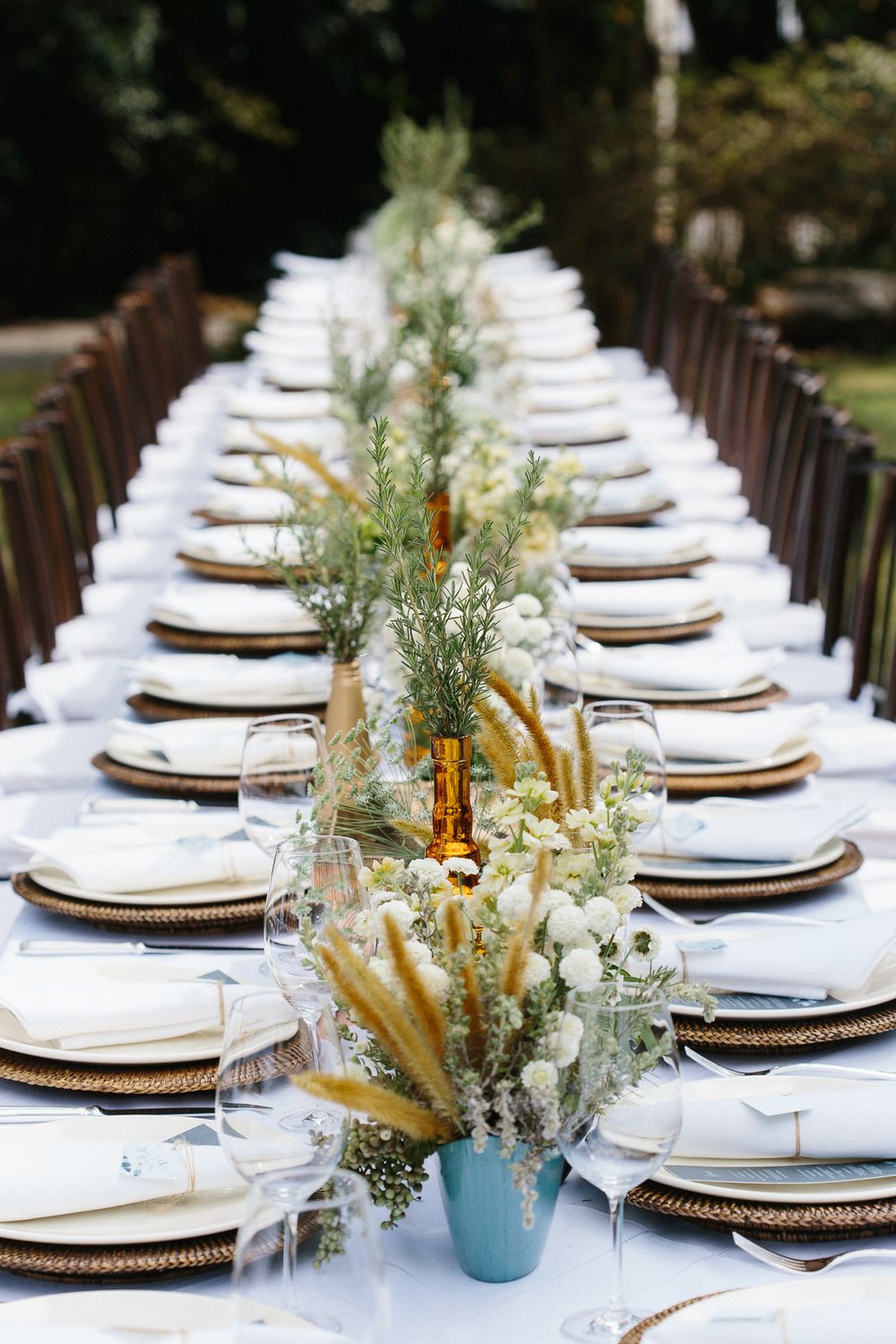 Elegant table setting with white linens, gold chargers and greenery centerpieces for a wedding reception.