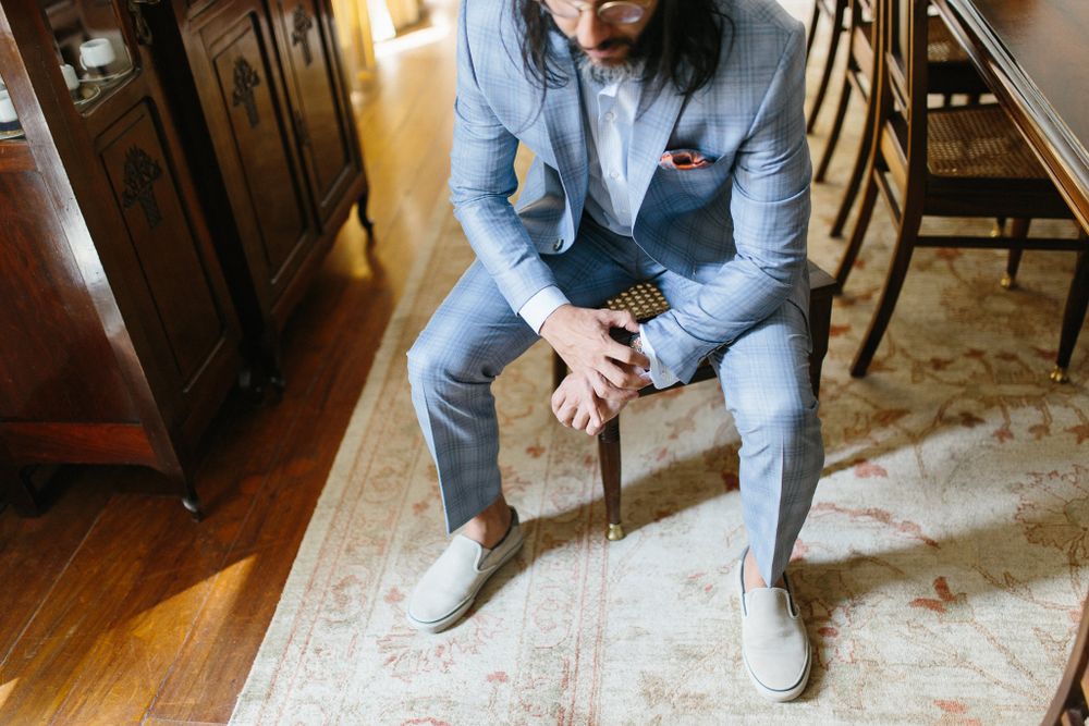 Person in gray suit seated on wooden chair in formal interior setting.