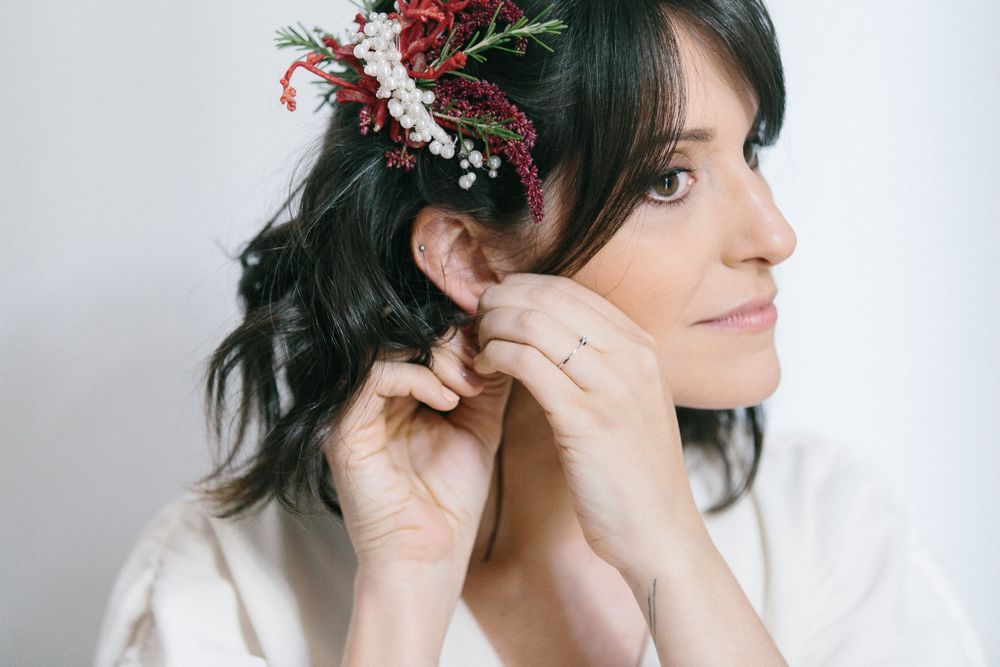 Close up shot of person wearing a delicate floral hair accessory and white robe while putting on earrings.