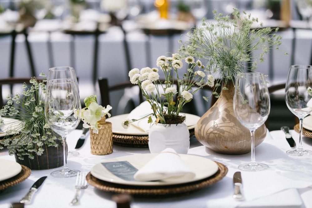 Elegant wedding table setting with white flowers and gold vases on a crisp white tablecloth.