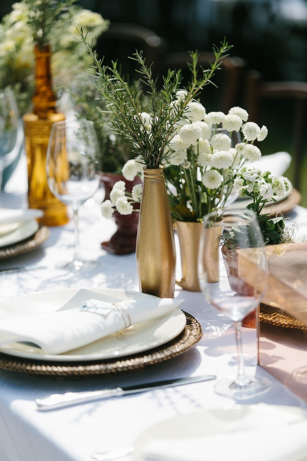 Table decor with metallic gold vases filled with white flowers and greenery.