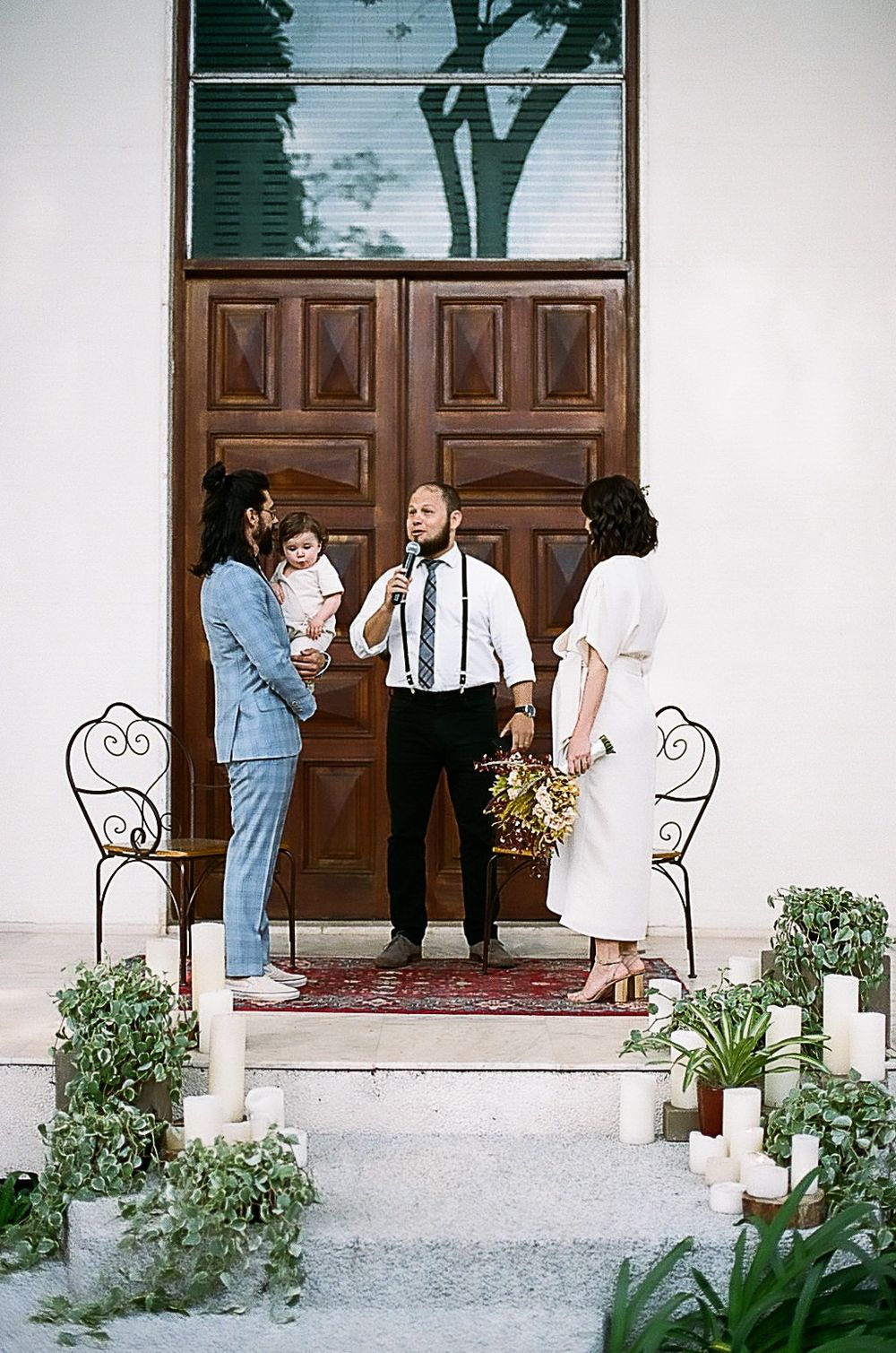 Group gathered on church steps with wooden doors and potted plants.
