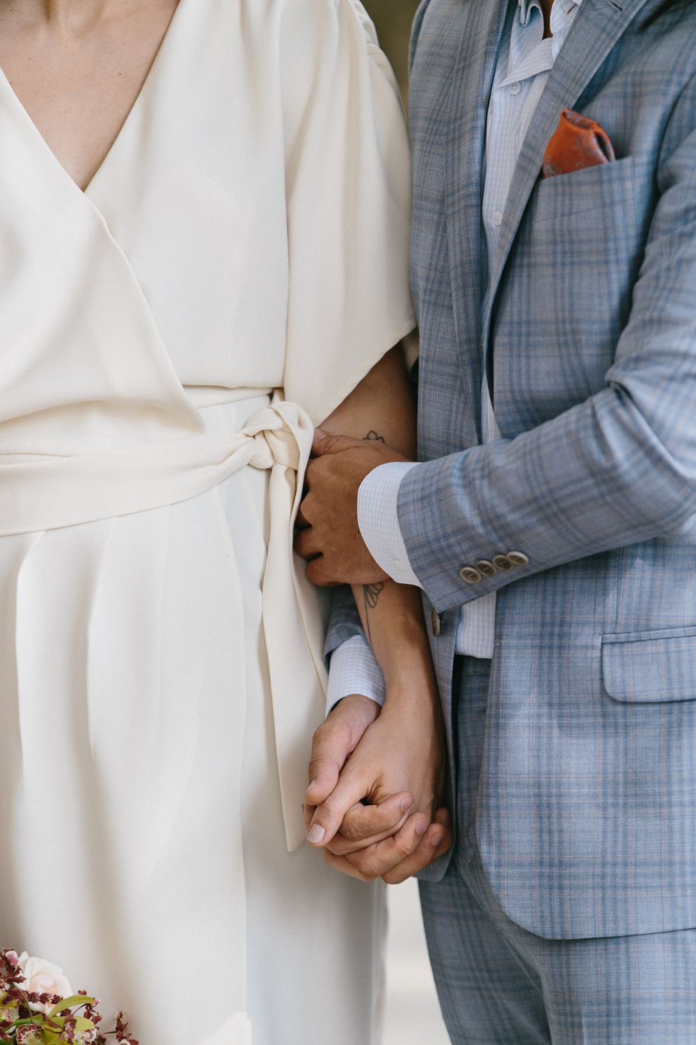 Close-up of couple holding hands, showing cream dress and blue checkered suit details.