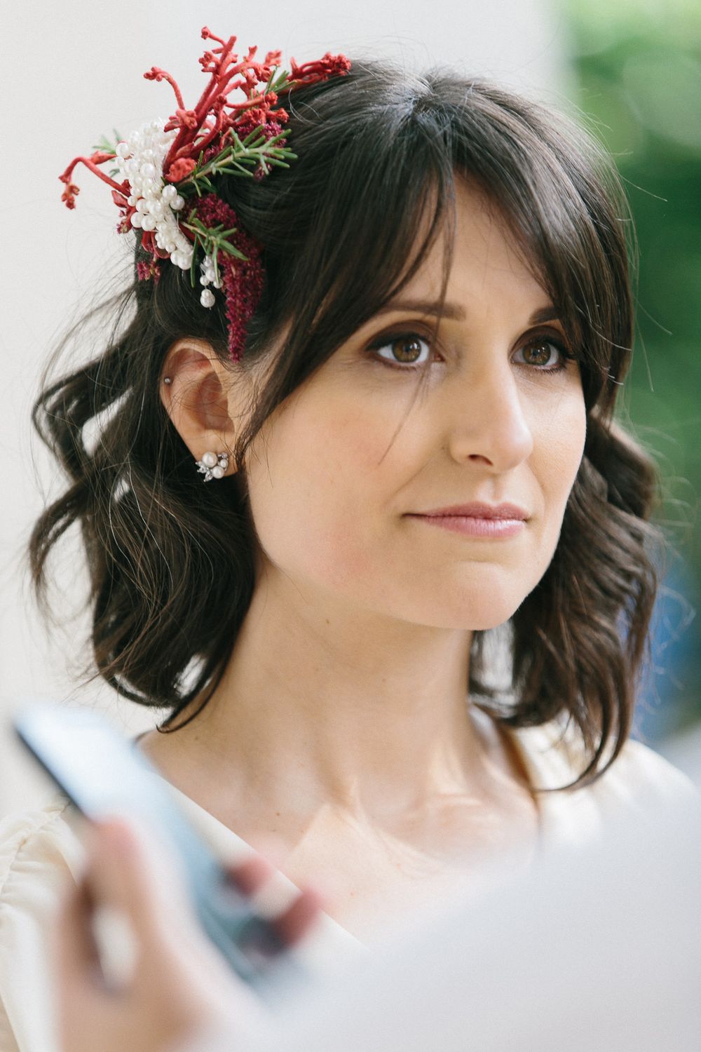 Close up of wavy dark hair adorned with red and white floral hair piece and delicate earrings.