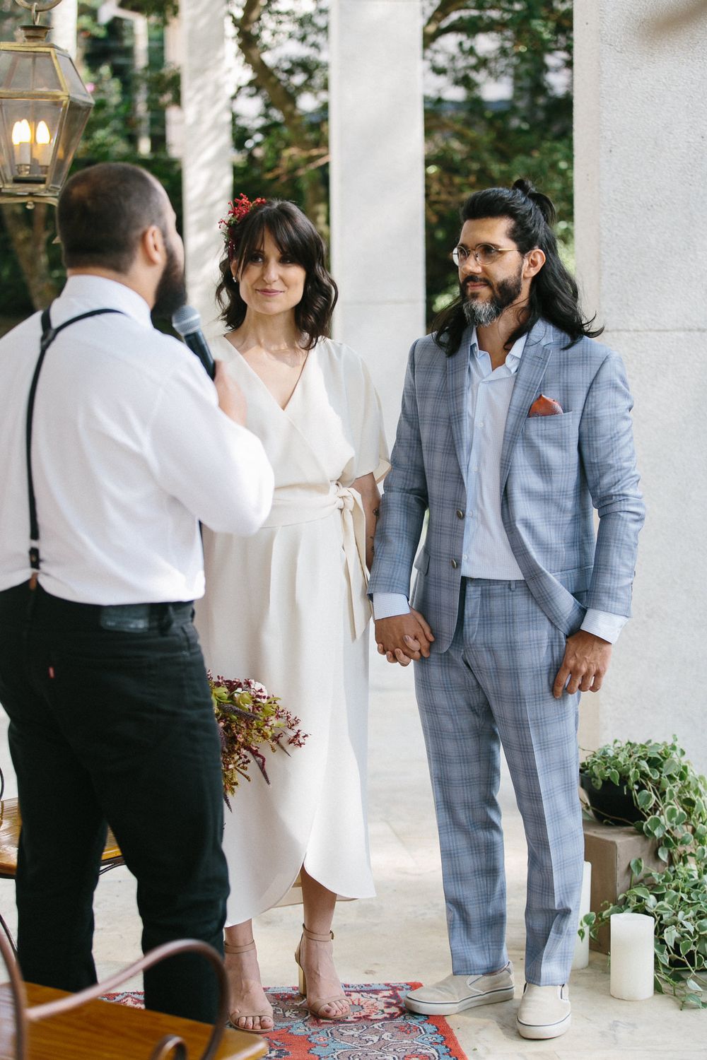 A couple stands with an officiant on a porch during their intimate wedding ceremony.