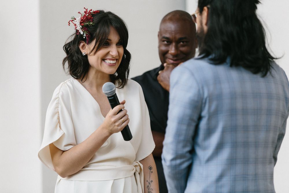 A couple exchanges vows during an intimate wedding ceremony with a microphone at an indoor venue.