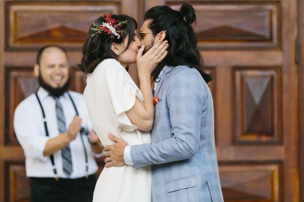 A romantic wedding kiss moment captured in front of wooden doors with an officiant in the background.
