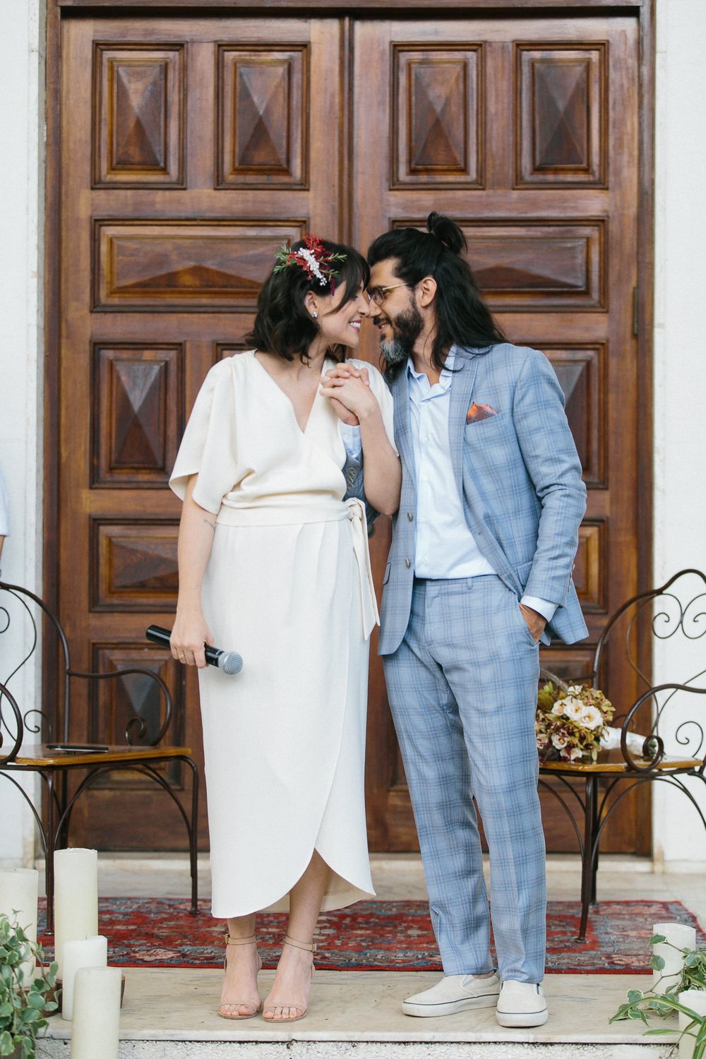 A tender moment between newlyweds standing against ornate wooden doors with decorative candles.