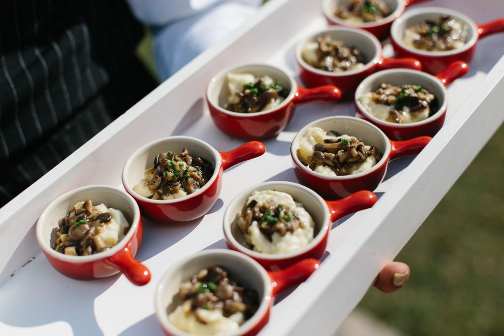 Red ceramic cups filled with appetizers arranged neatly on a white serving tray.