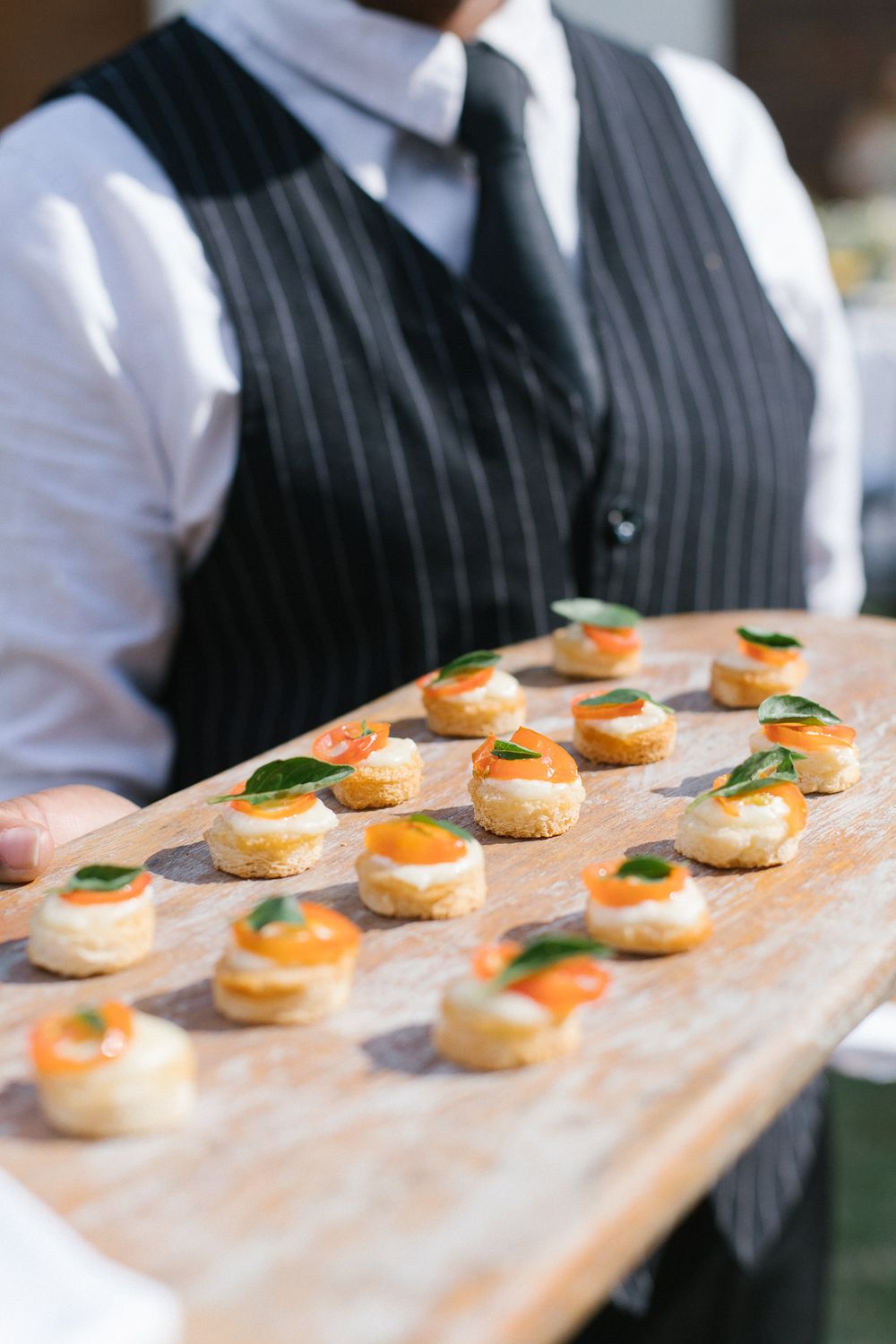 Server holding wooden board with elegant smoked salmon canapes garnished with fresh herbs.