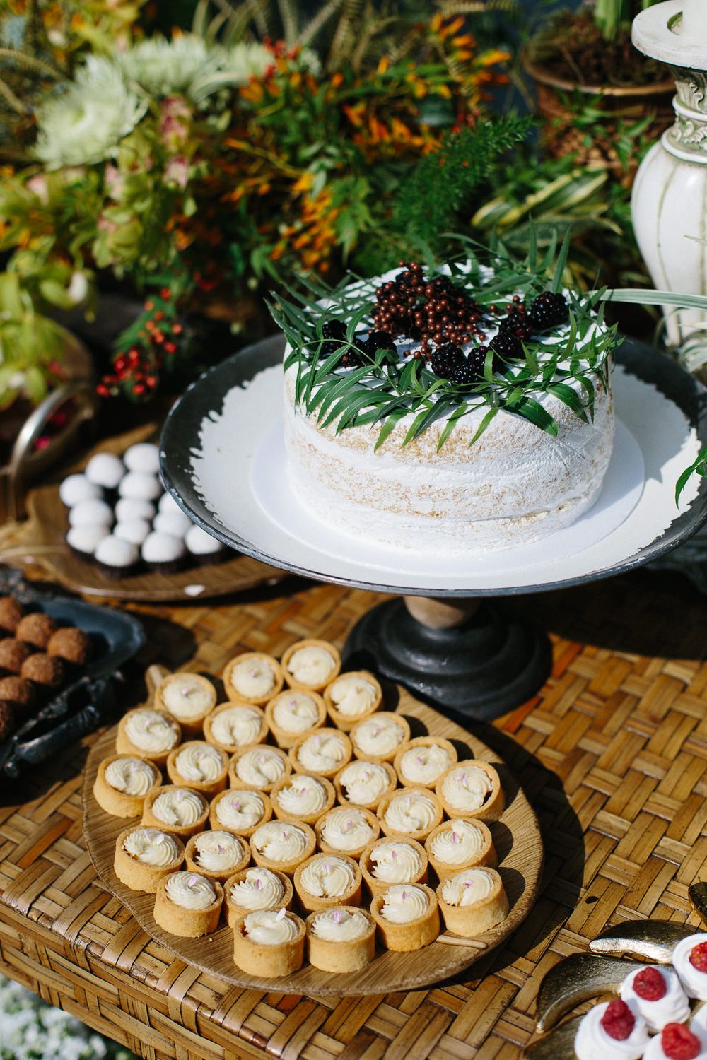 White frosted cake decorated with greenery on cake stand alongside assorted desserts.