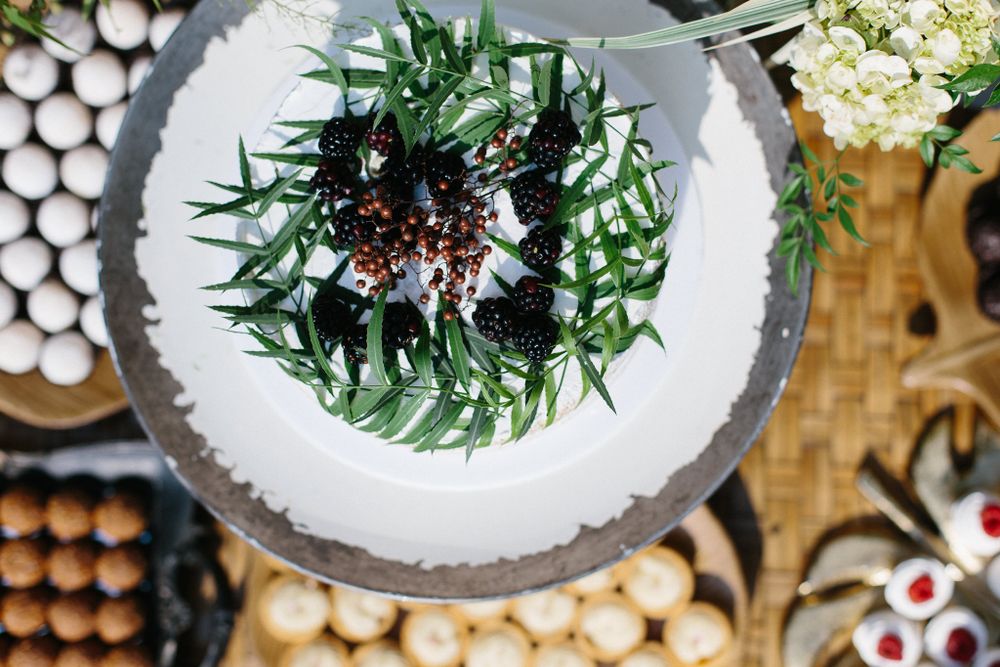 Overhead view of white cake decorated with dark berries and fresh greenery.