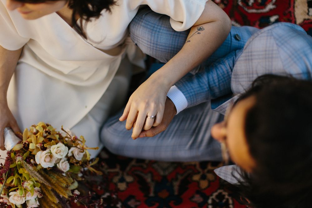 Close-up view of two people sitting on a patterned rug with flowers between them.