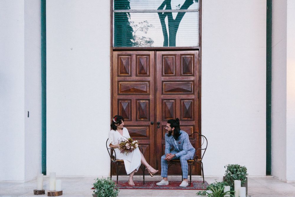 Couple in white and blue outfits sitting together on steps outside a building with wooden doors.