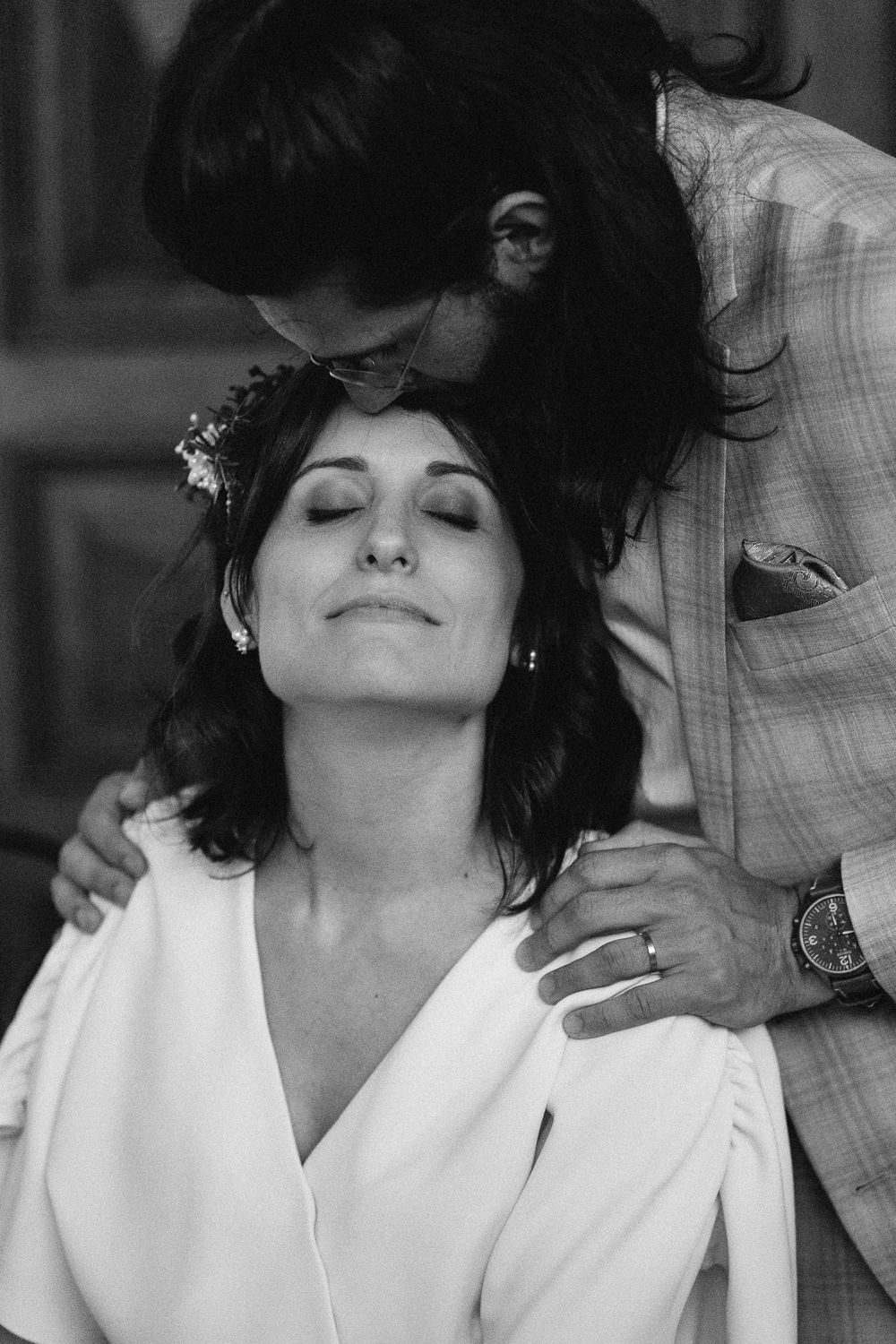 Woman in white robe with floral hair accessory smiles serenely during wedding preparation.