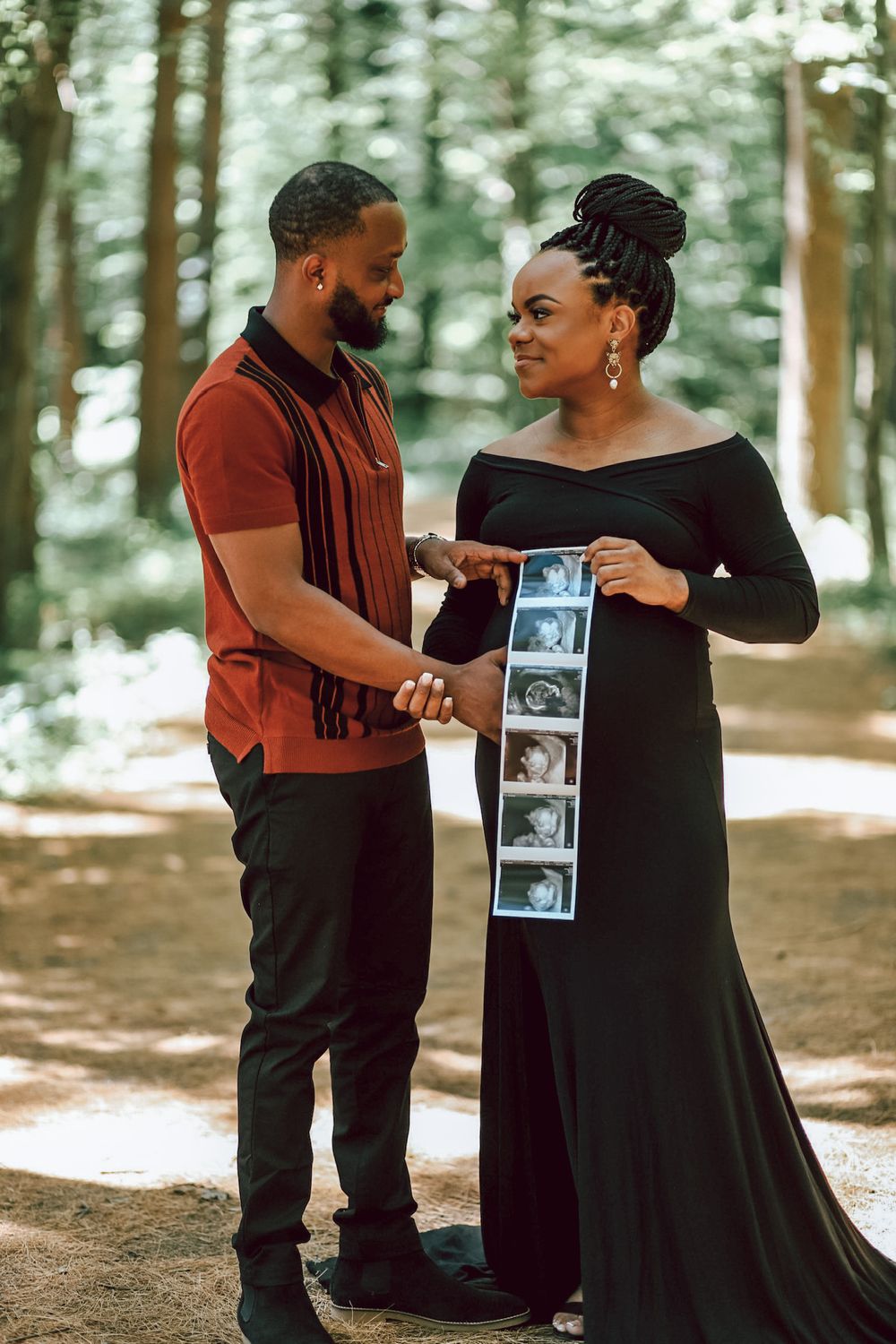 A couple poses lovingly in a forest while holding sonogram photos during a pregnancy announcement photoshoot.