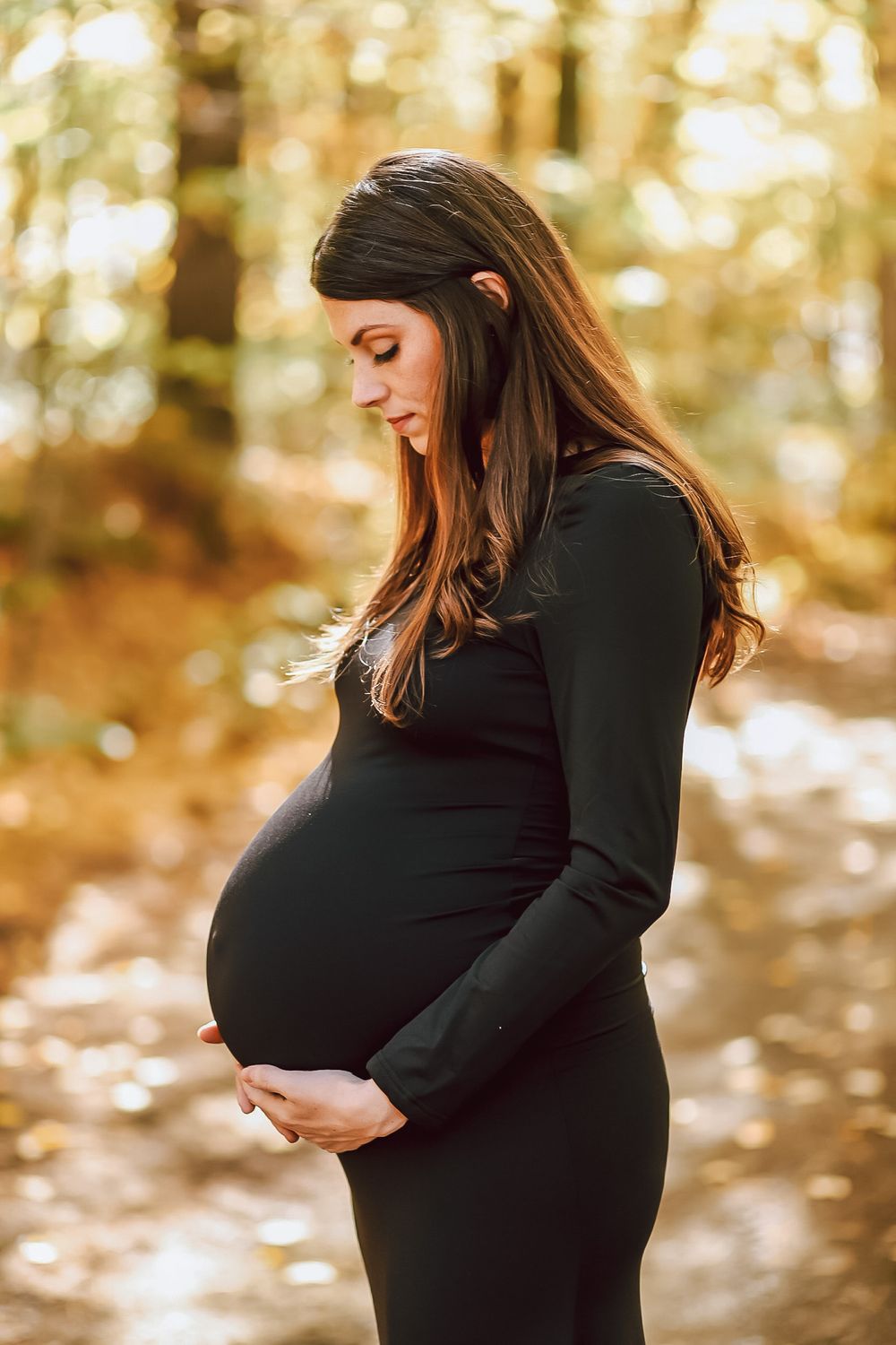 Outdoor maternity photos in black dress showing baby bump silhouette against autumn foliage.