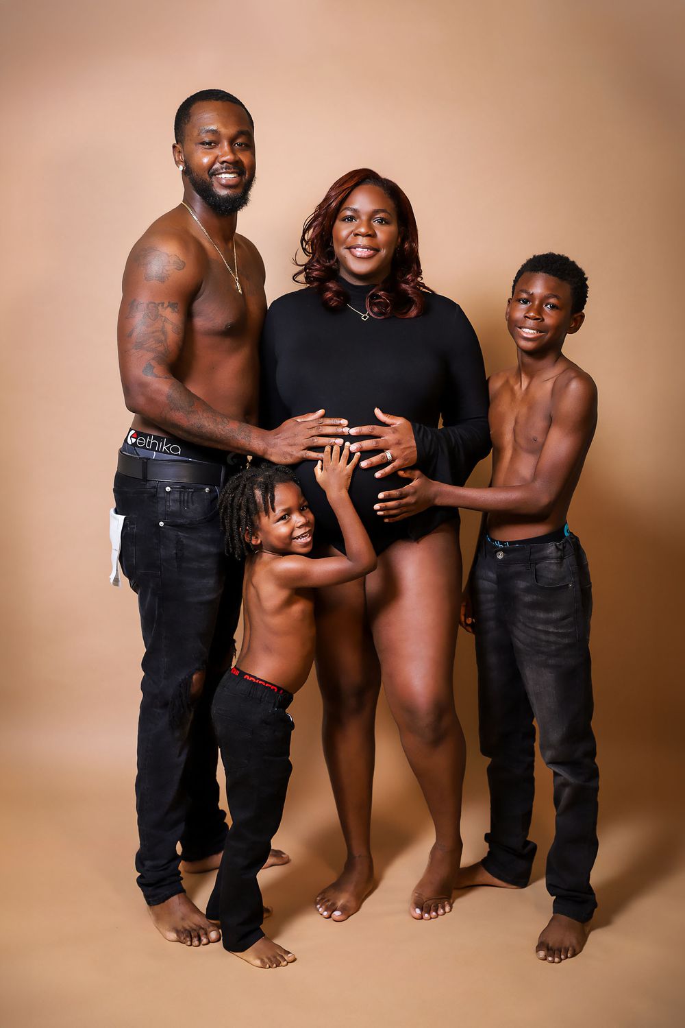 Family maternity photoshoot showing a baby bump celebration against a warm brown backdrop.