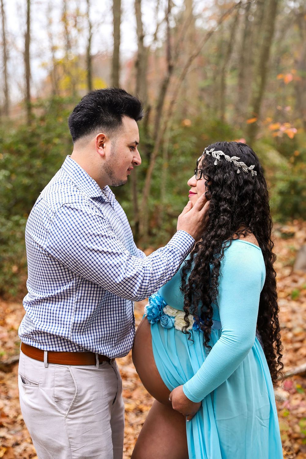 Romantic maternity photo of couple in autumn forest with woman in blue dress.