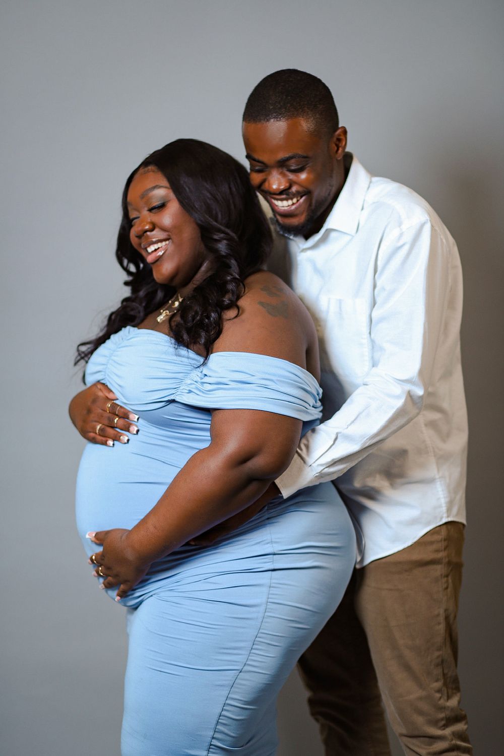 Joyful maternity portrait of couple embracing in blue dress and white shirt.